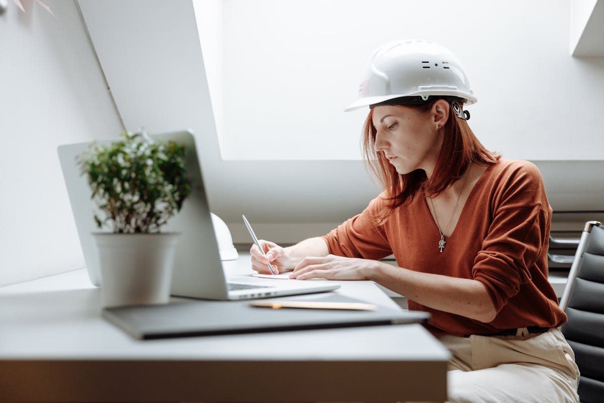 Handwerkerin mit Schutzhelm erstellt ein Angebot am Laptop