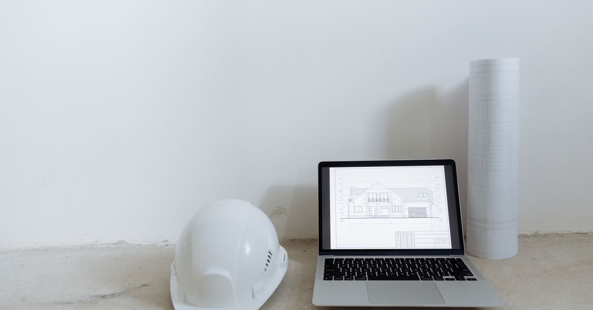 Laptop mit Bauplan, Schutzhelm und Planrolle im Rohbau als digitale Grundlage für das Leistungsverzeichnis Elektro